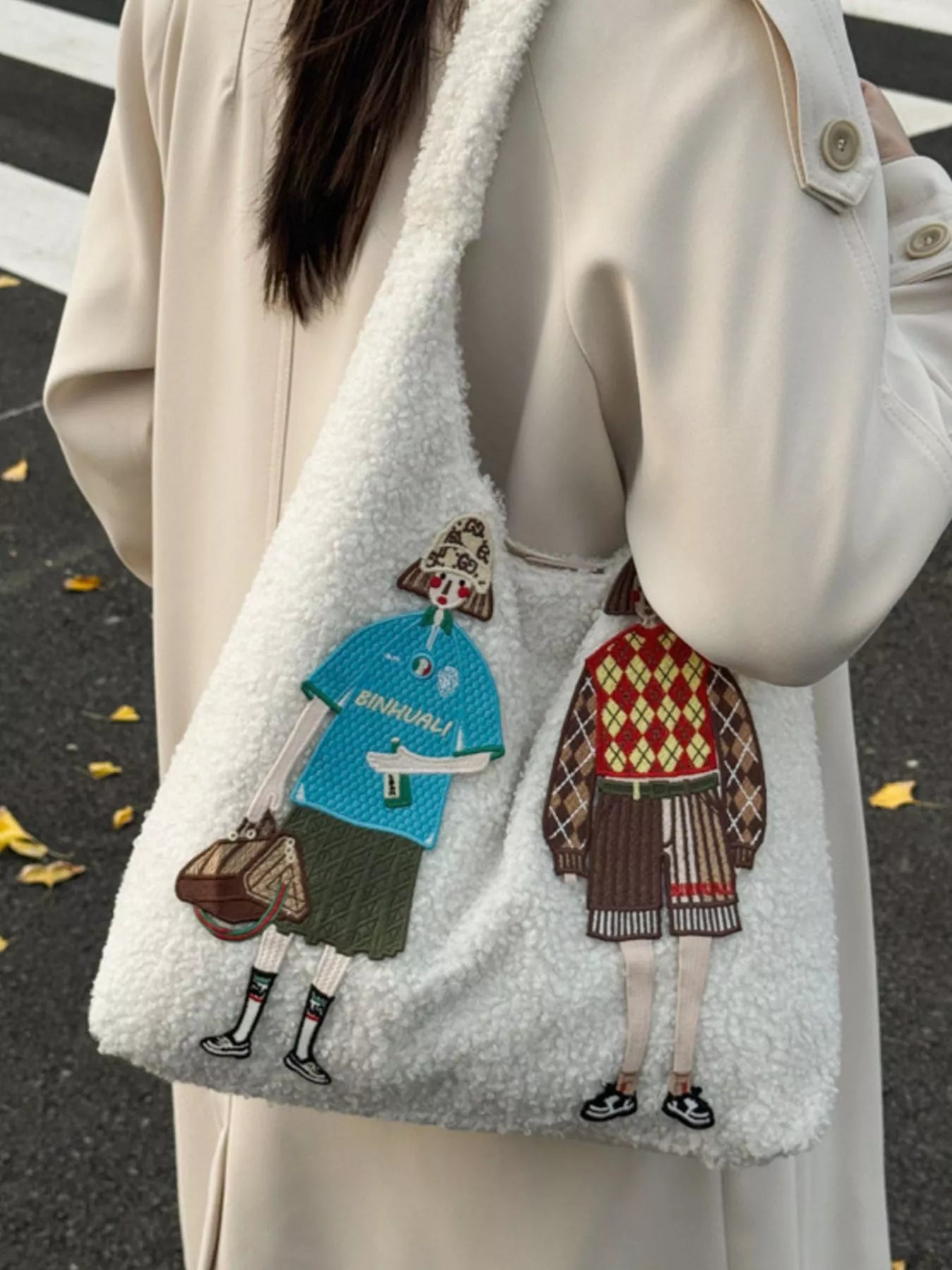 Person wearing a coat with a white fleece-lined hood, carrying a tote bag with embroidered characters.