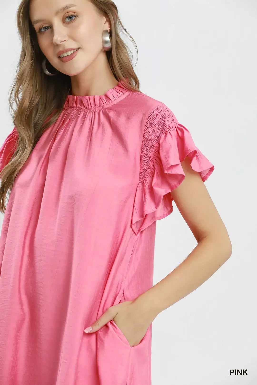 Woman wearing a pink dress with ruffled sleeves on a white background