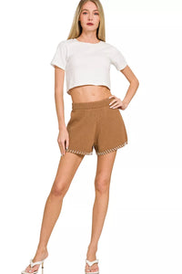 Woman wearing a white crop top and brown shorts on a white background