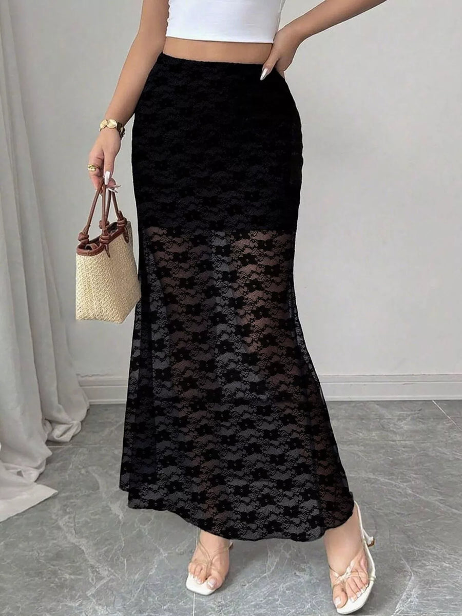 Person wearing a black lace skirt with a white top and sandals, holding a straw bag.