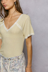 Woman wearing a light yellow ribbed top with lace trim against a gray background
