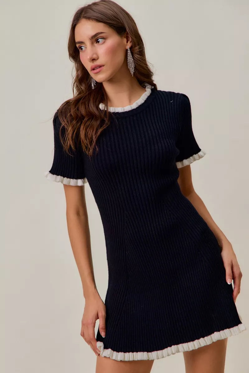 Woman wearing a black ribbed dress with white trim on a plain background
