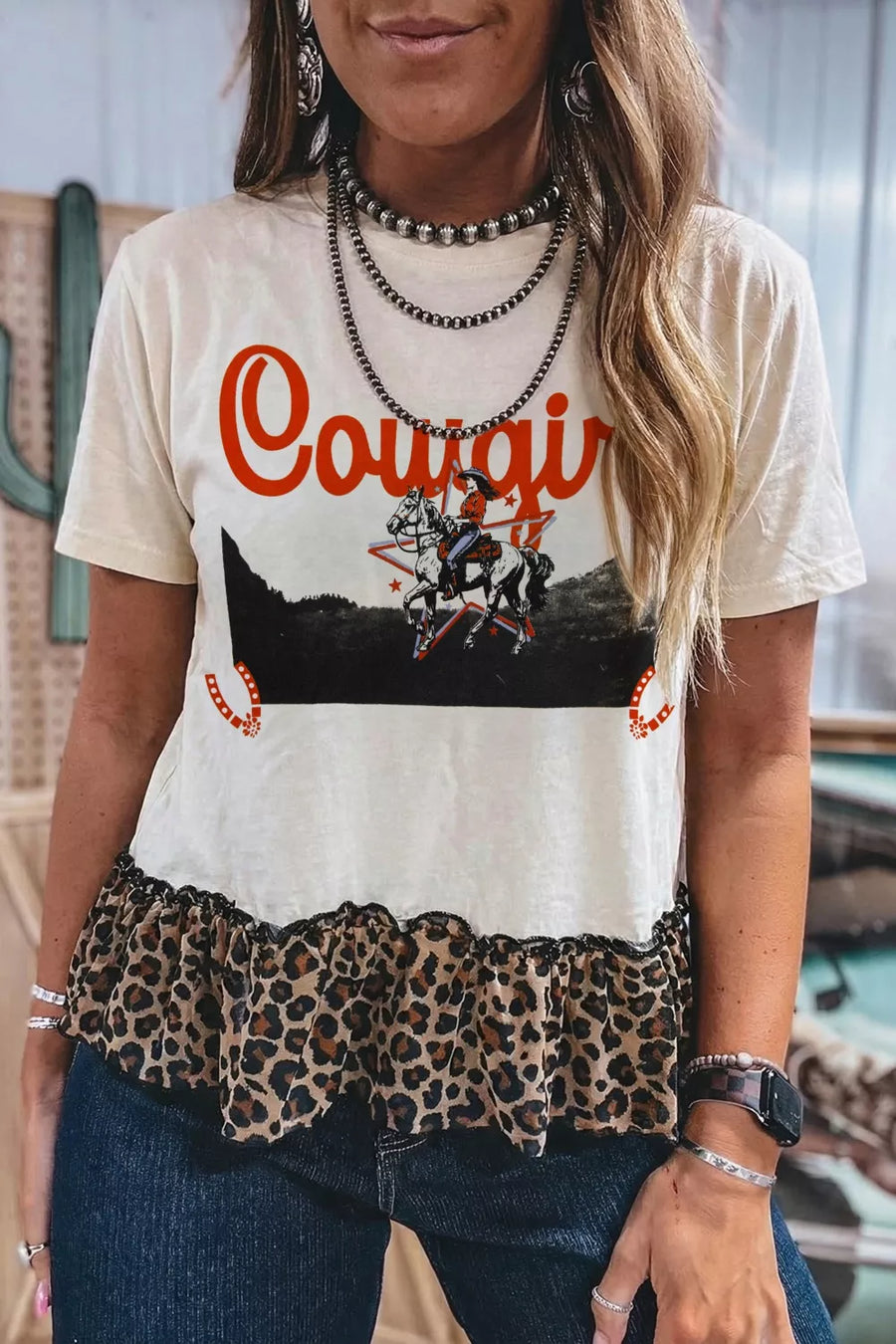 Person wearing a t-shirt with 'Cowgirl' graphic and leopard print trim.