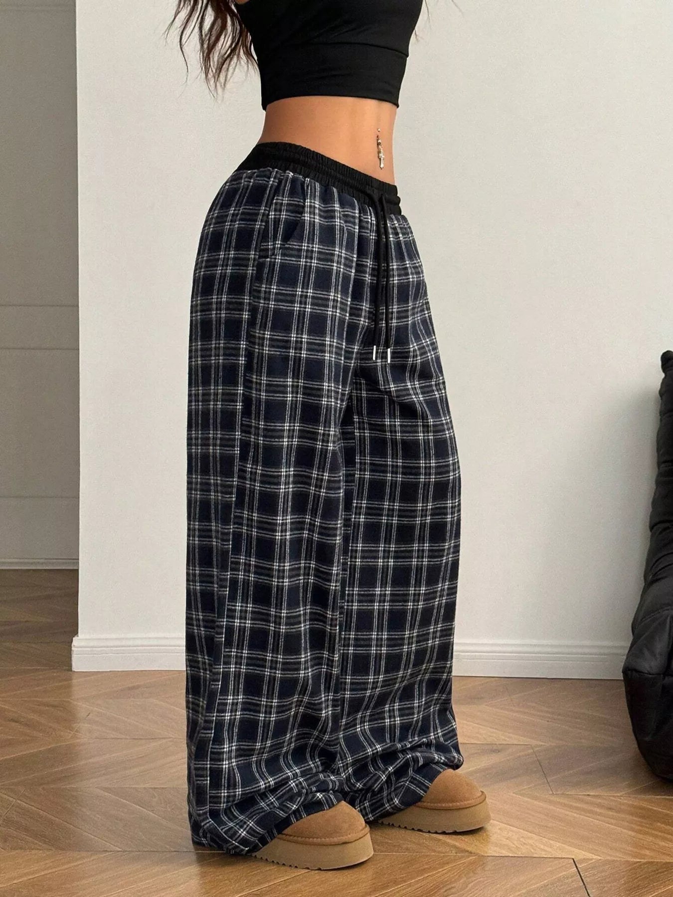 Person wearing plaid pants and black top on a wooden floor.