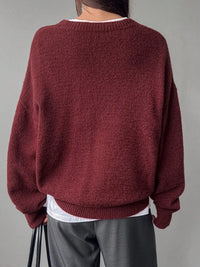 Maroon sweater worn by a person on a gray background