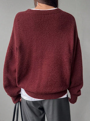 Maroon sweater worn by a person on a gray background