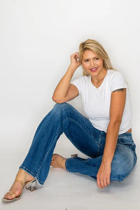 Woman wearing a white t-shirt and blue jeans sitting on a light gray background