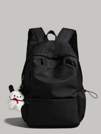 Black backpack with a small white plush toy attached on a gray background