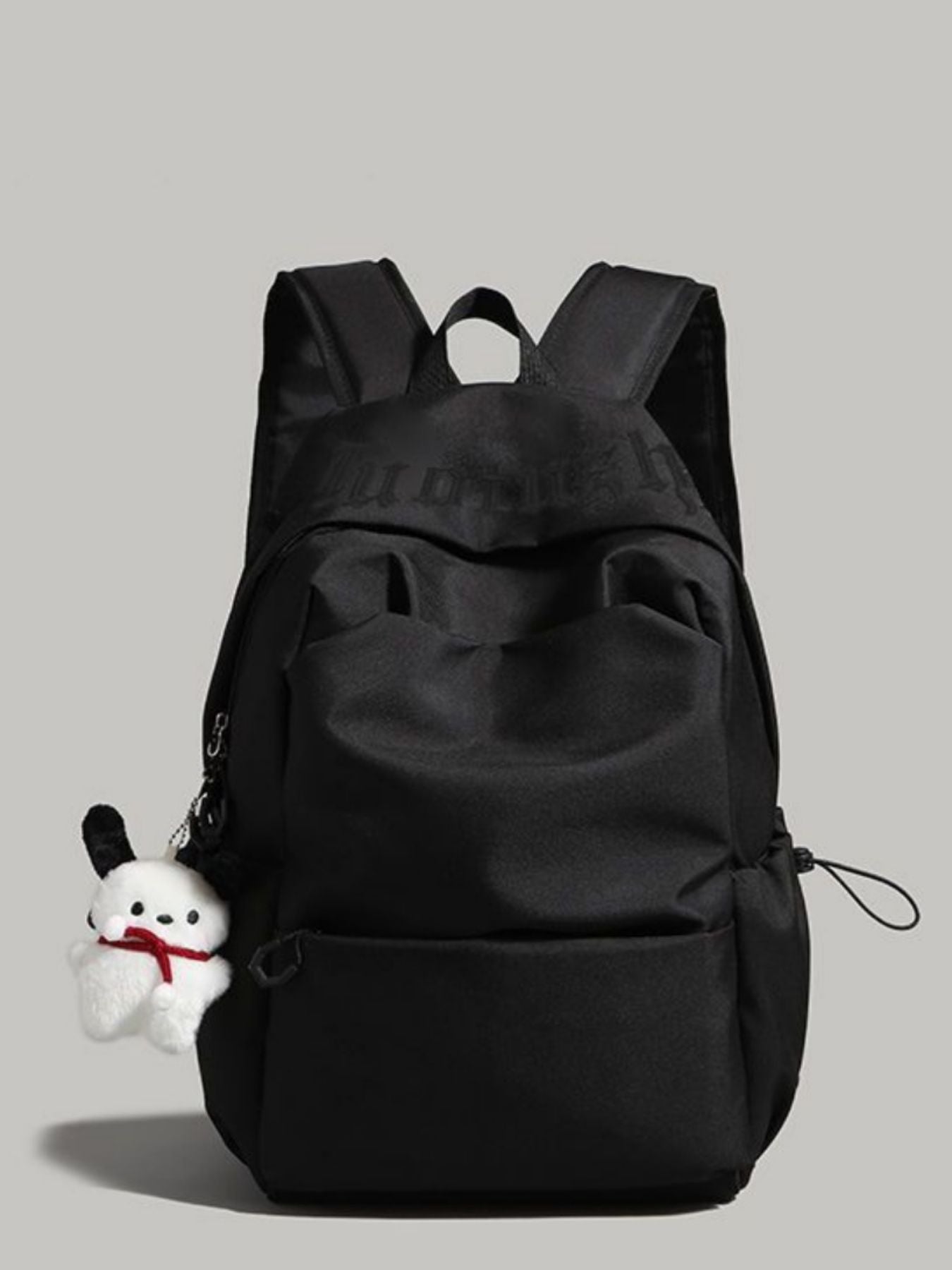 Black backpack with a small white plush toy attached on a gray background