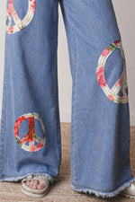 Blue jeans with peace symbol patches on a neutral background