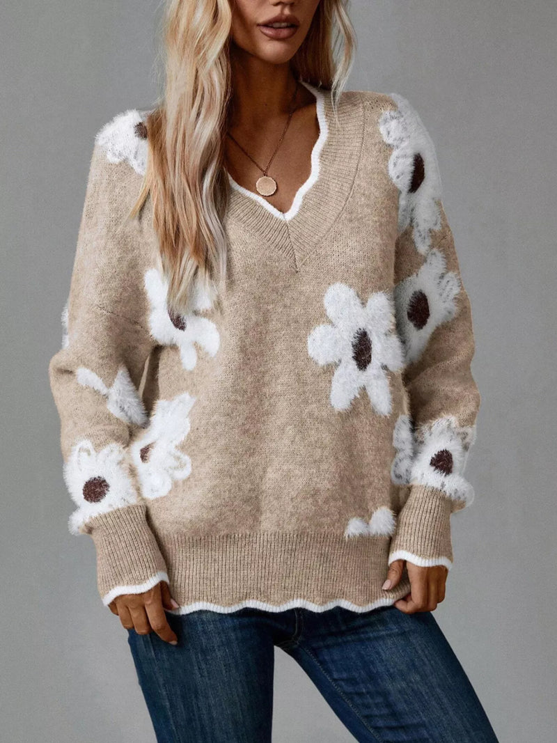 Beige sweater with white floral patterns worn by a person on a gray background