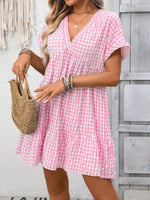 Woman wearing a pink checkered dress holding a woven bag against a gray wooden background