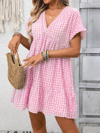 Woman wearing a pink checkered dress holding a woven bag against a gray wooden background