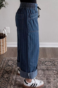 Person wearing blue striped pants standing on a patterned rug indoors.