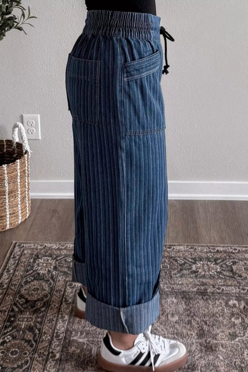 Person wearing blue striped pants standing on a patterned rug indoors.