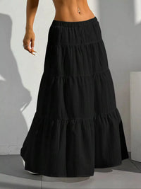 Black tiered skirt worn by a person against a white wall.