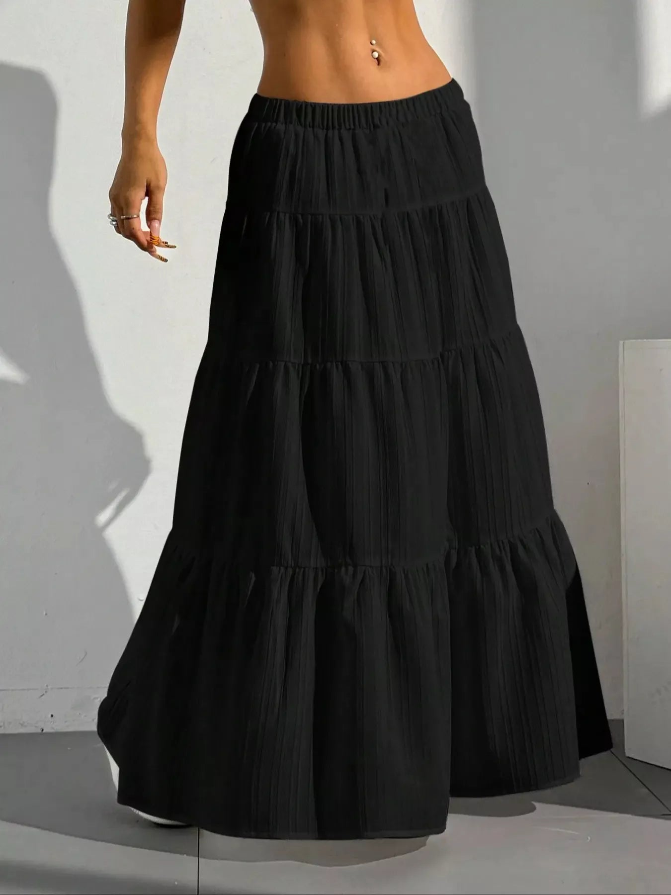 Black tiered skirt worn by a person against a white wall.