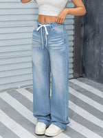 Person wearing light blue wide-leg jeans and white sneakers on a striped floor.