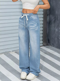 Person wearing light blue wide-leg jeans and white sneakers on a striped floor.