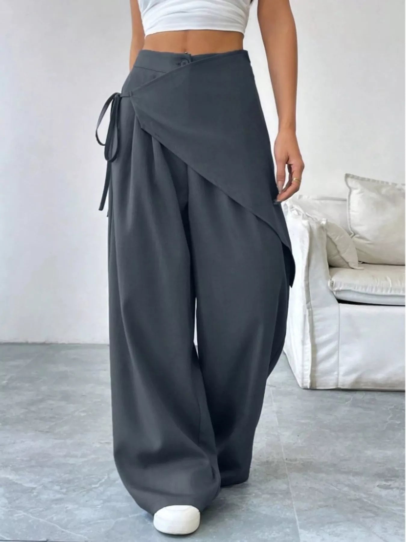 Person wearing gray wide-leg pants with a white top in a minimalistic room.
