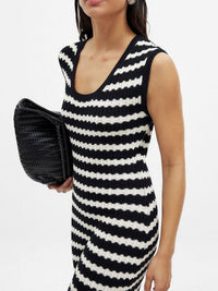 Woman wearing a black and white striped dress holding a black clutch against a white background