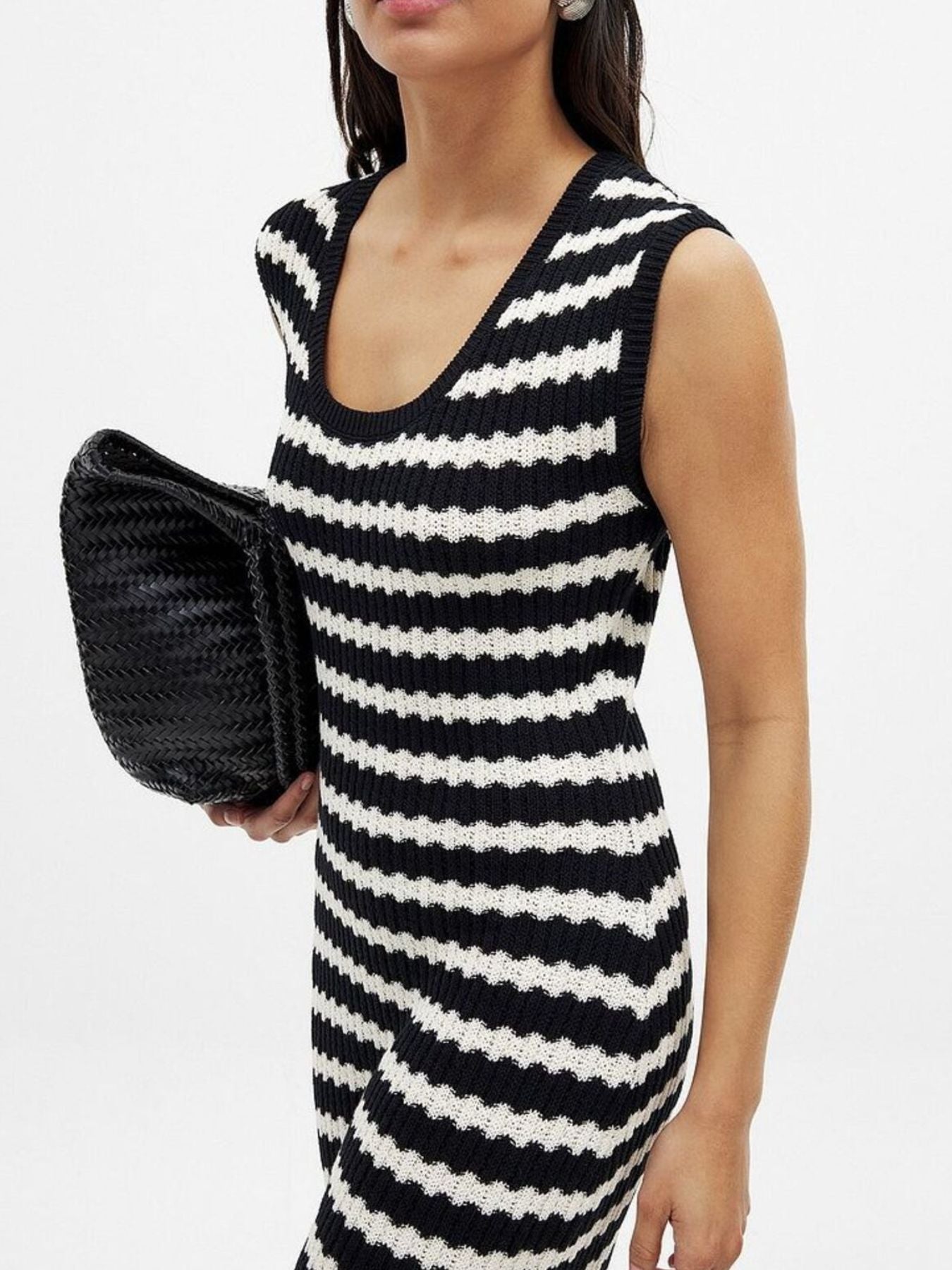 Woman wearing a black and white striped dress holding a black clutch against a white background