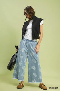 Woman wearing a black sleeveless jacket, white shirt, and light blue pants with a pattern on a green background