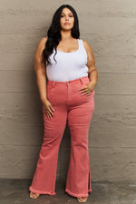 Woman wearing a white tank top and pink flared jeans against a gray wall.
