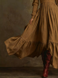 Person wearing a long brown dress with a flowing skirt and red boots against a dark background
