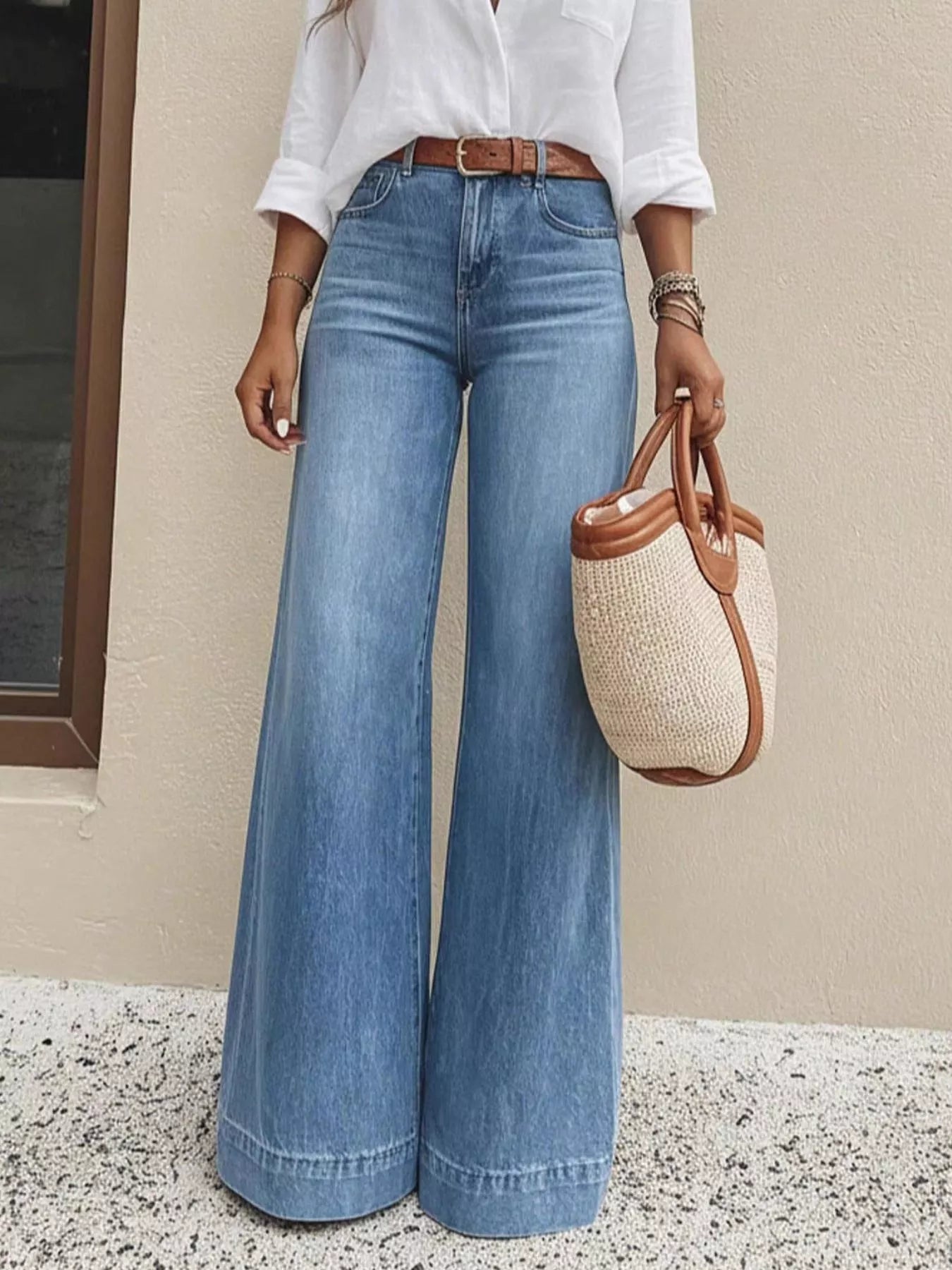 Person wearing blue jeans and a white shirt, holding a woven handbag.