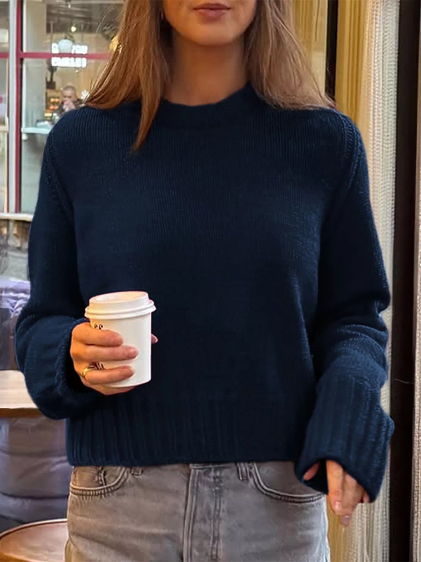 Person wearing a navy sweater holding a white coffee cup indoors.