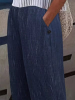 Close-up of a person wearing wide-leg blue pants with a subtle vertical textured stripe pattern, a white top with thin black stripes, and a hand in a pocket near a button closure.