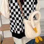 Fluffy white swan-shaped handbag with yellow feet held by a person wearing a black and white checkered sweater.