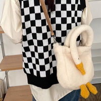 Fluffy white swan-shaped handbag with yellow feet held by a person wearing a black and white checkered sweater.