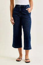 Person wearing dark blue jeans on a plain background