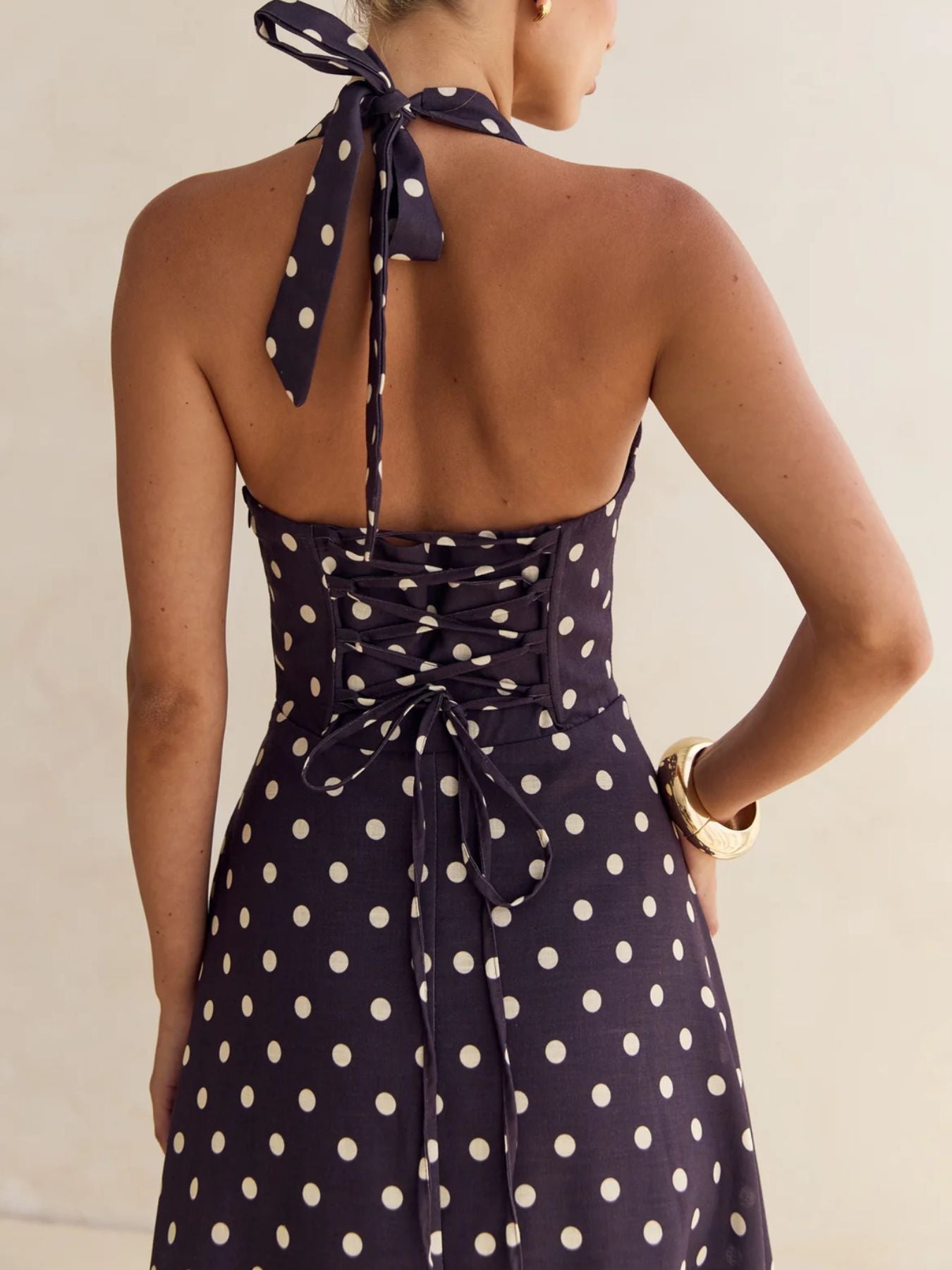 Navy blue dress with white polka dots featuring a halter neck design on a neutral background