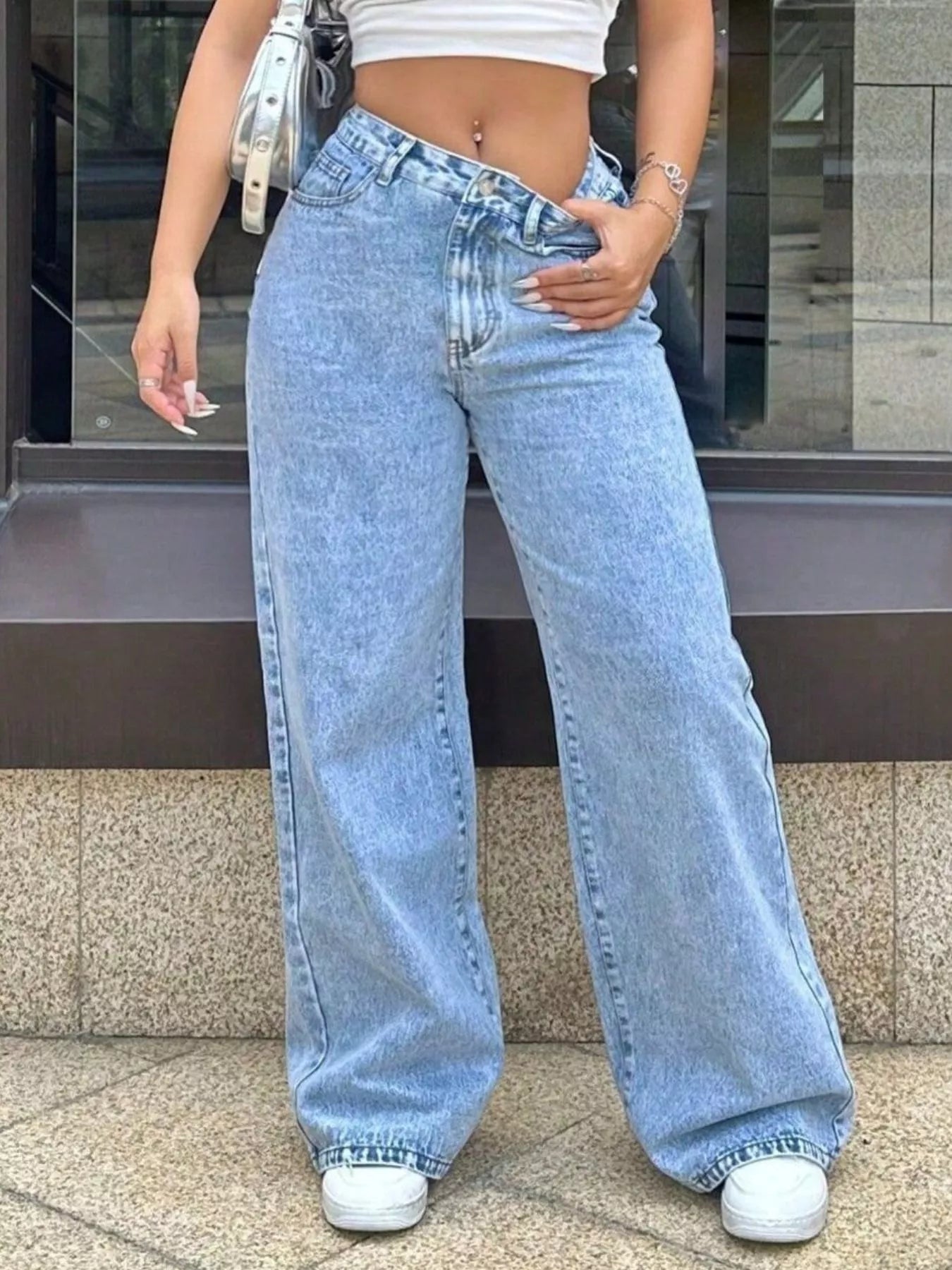 Person wearing light blue jeans and a white crop top standing on a sidewalk.