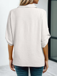 Person wearing a light-colored shirt with rolled-up sleeves against a neutral background