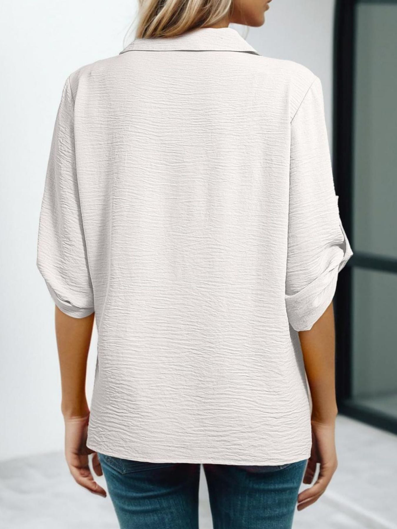 Person wearing a light-colored shirt with rolled-up sleeves against a neutral background