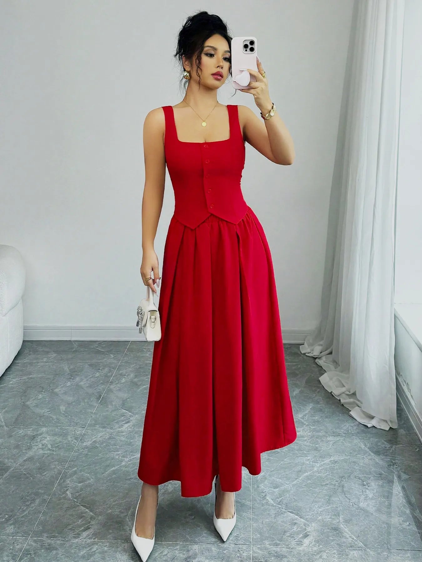 Woman taking a mirror selfie wearing a red dress in a room with white walls and gray floor.
