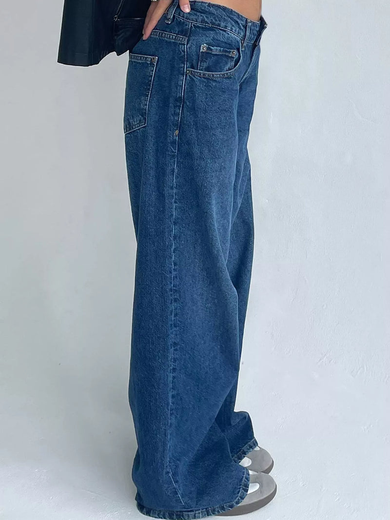 A person wearing wide-leg blue denim jeans, shown from the waist down against a plain light gray wall.