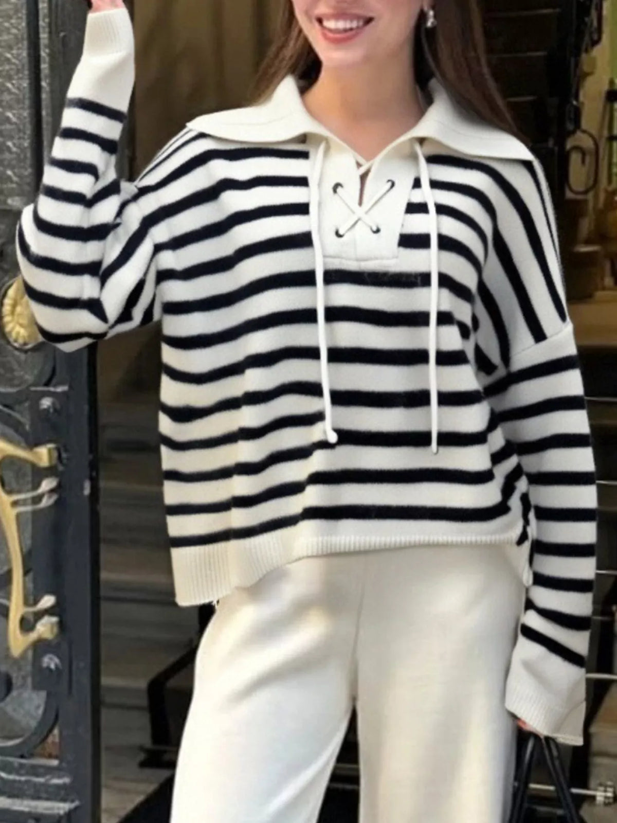 Person wearing a black and white striped sweater with a lace-up front, standing indoors.