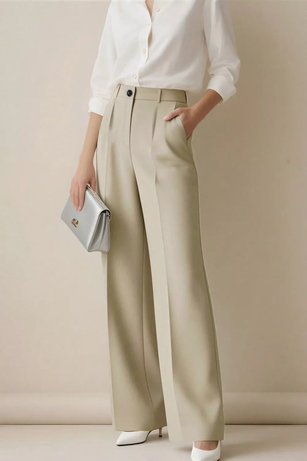 Person wearing a white shirt and beige wide-leg pants holding a silver clutch against a plain background