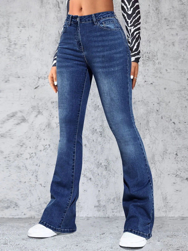 Person wearing blue flared jeans against a gray concrete wall.