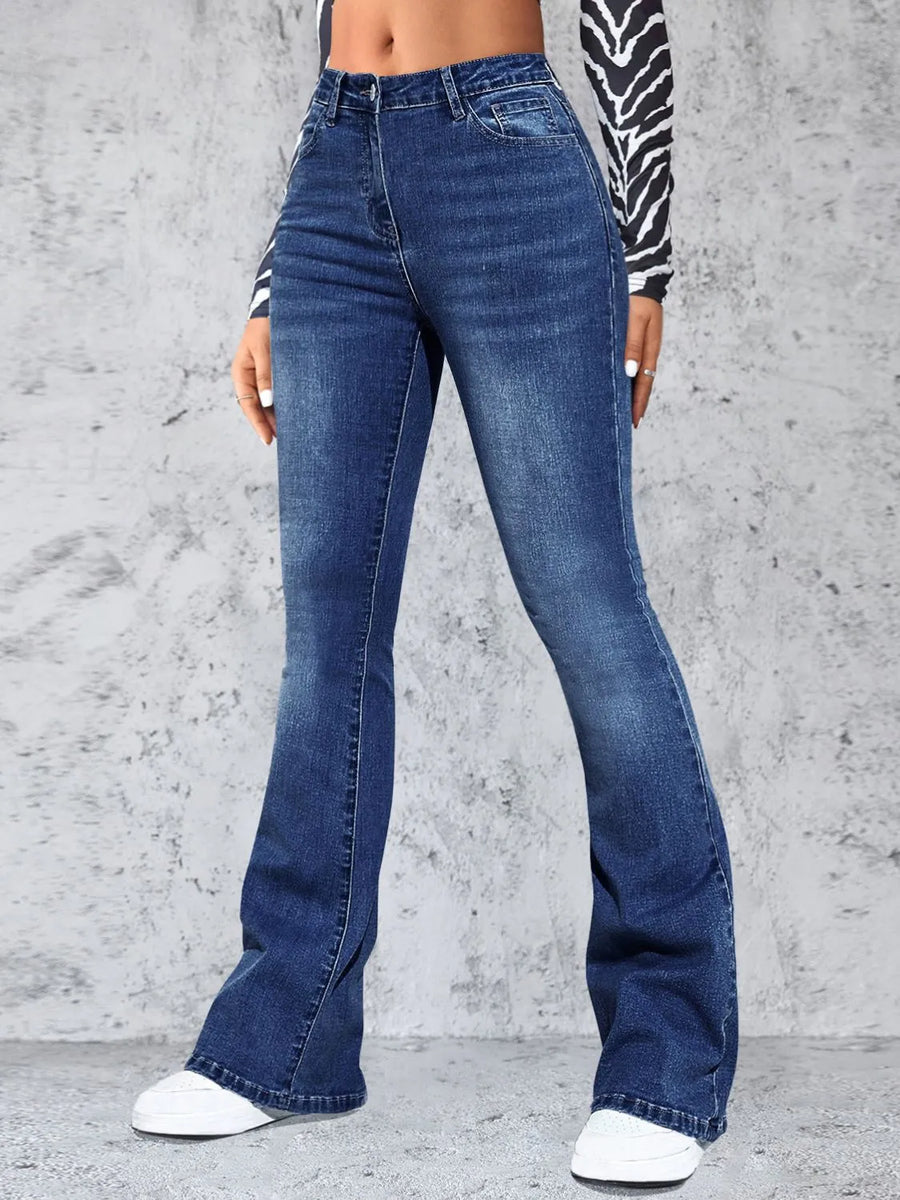 Person wearing blue flared jeans against a gray concrete wall.