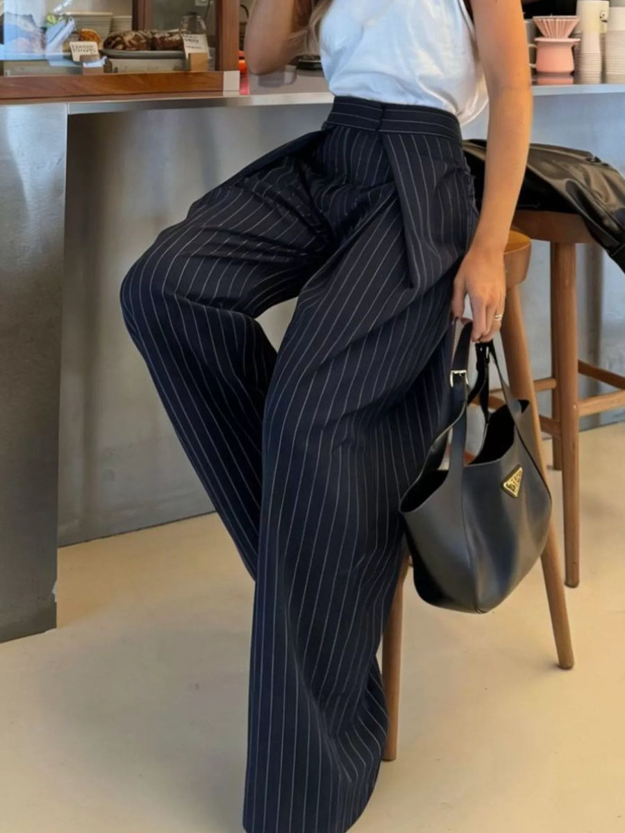 Person wearing pinstripe pants sitting on a stool indoors.