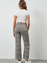 Person wearing leopard print pants and a white top against a plain background
