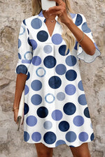 Woman wearing a polka dot dress with blue and white pattern against a stone wall.