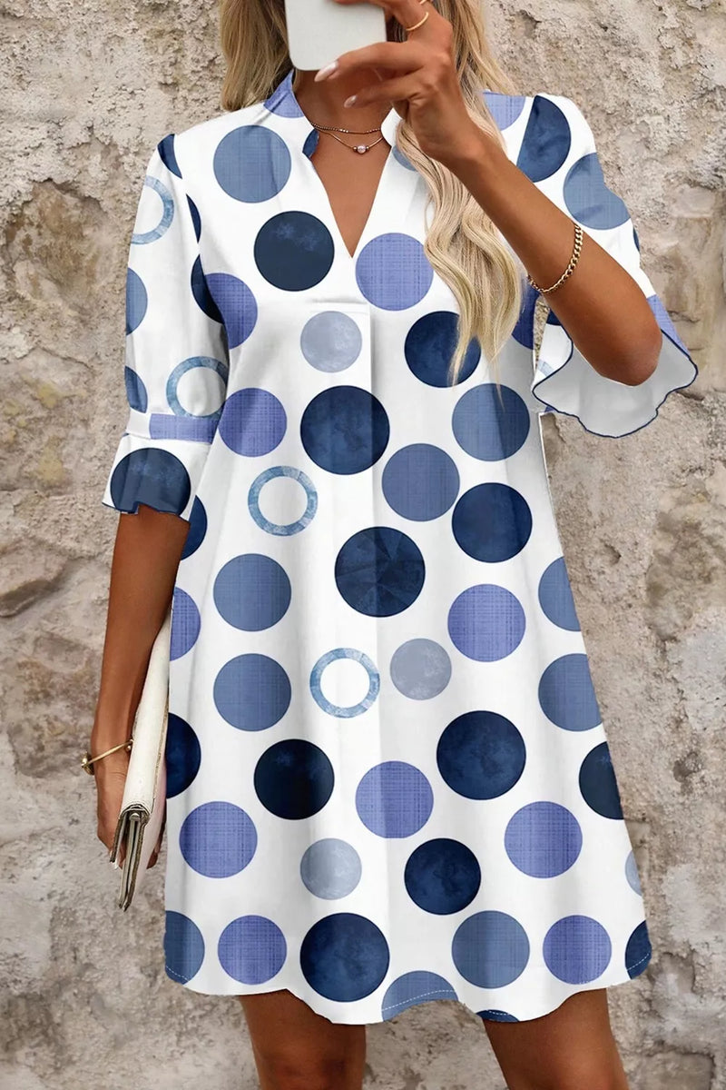Woman wearing a polka dot dress with blue and white pattern against a stone wall.