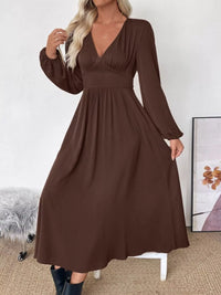 Woman wearing a brown dress with long sleeves in a minimalistic room.